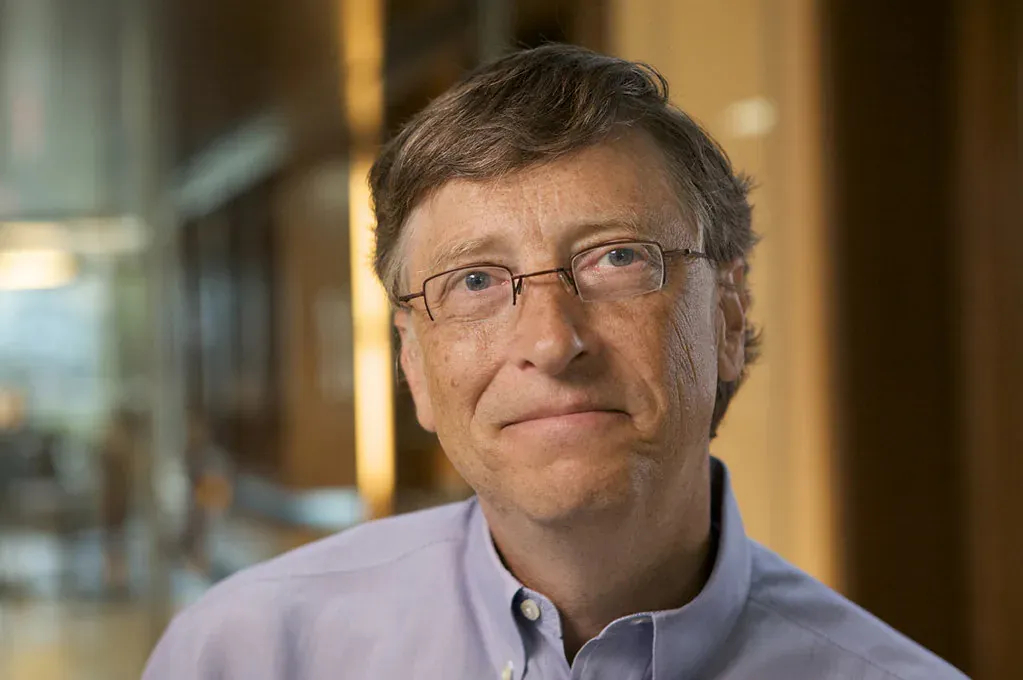 Bill Gates from the shoulders up in glasses and a pale blue shirt, smiling slightly at the camera.