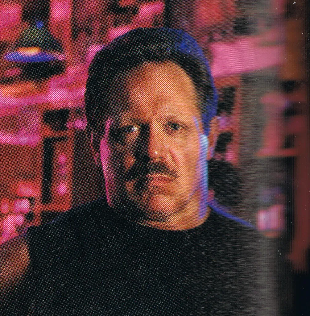 Christopher Langan from the chest up in a black sleeveless top, photographed against a magenta and blue backdrop.